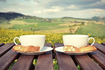Filtered image of two coffee cups and cantuccini on the wooden t
