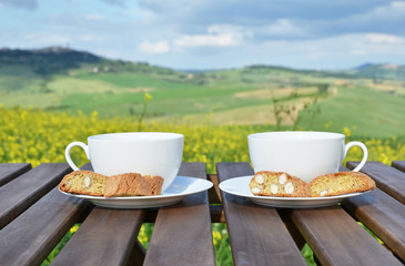 Two coffee cups and cantuccini on the wooden table against Tusca