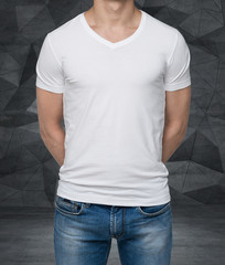 Close up of the body view of the man in a white t-shirt. Hands are crossed behind the back. Contemporary office background.