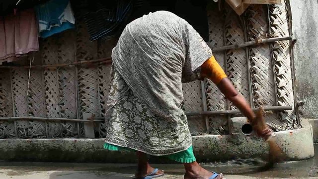 Inde. Quartier populaire, femme qui balaie