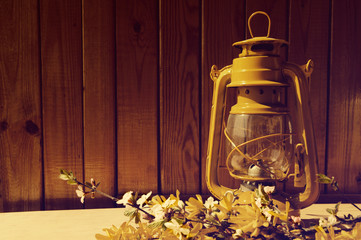 Yellow oil lamp and bouquet of spring yellow Forsythia colors against a wooden wall. A spring still life with an oil lamp.
