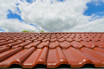 Naklejka premium Close-up of glazed brown roof tiles against blue cloudy sky background