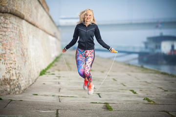 Woman exercising outdoors with a jump rope - obrazy, fototapety, plakaty
