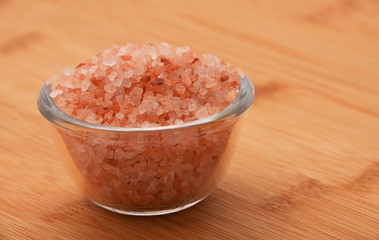 Himalayan pink salt in tiny transparent glass bowl on wooden bam