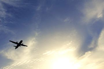 Silhouette of an airplane flying in the blue sky with white clouds