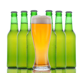A cold frosty glass of beer in front of a group of green bottles on a white background. Horizontal with reflection.