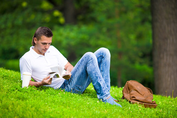 Naklejka na ściany i meble Young man relaxing with coffee in park reading a book