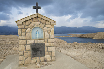 Obraz premium Marienfigur auf der Insel Pag mit dramatischem Himmel vor dem Velebit Gebirge