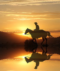 Reflection Cowboy.  A silhouette of a cowboy in a lake of yellow and gold colors.  The sun setting in the background.