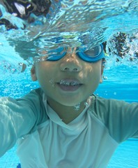 young 4 year old asian boy swims underwater half submerged