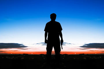 silhouette rear of man standing hand hold holding gun revolvers on sunrise and full moon on the sky in the city background