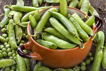 .peas in pods in ceramic bowl on a wooden table