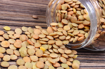 Lentil spilling out of glass jar. Wooden background