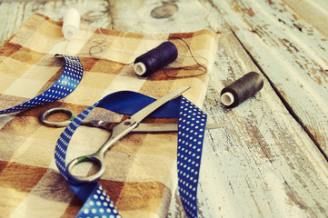 Scissors, threads, fabric and blue tape on a wooden textural table