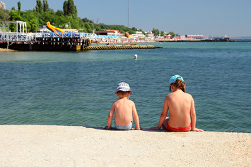 Children sitting back at the pier and watching the sea..