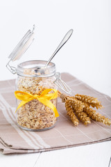 The oat flakes in glass jar with spoon and wheat.