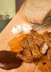 BBQ sauce with pork steak portion on wooden chopping board