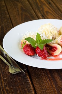 Two strawberries with melissa on plate with fruit dumplings