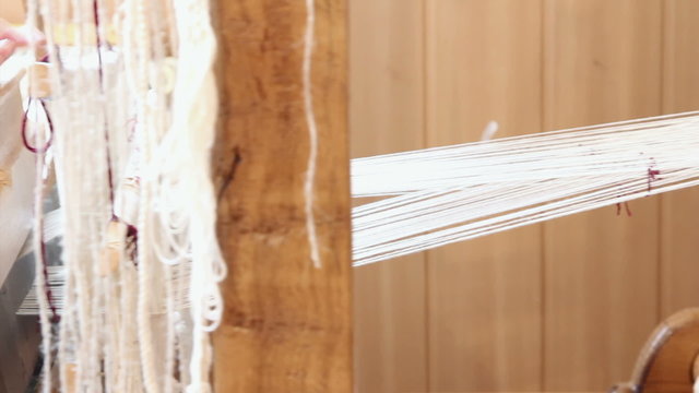 A woman weaves at an old wooden loom