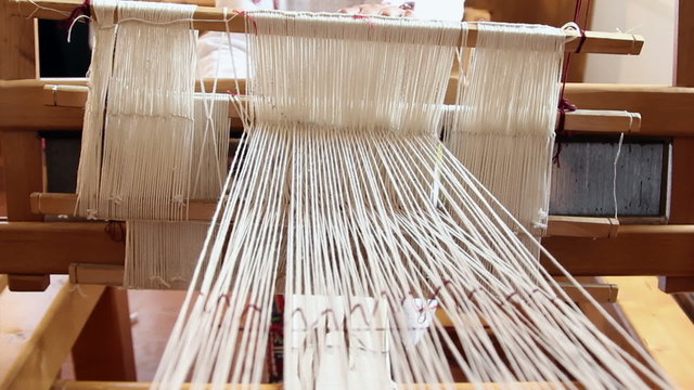 A woman weaves at an old wooden loom