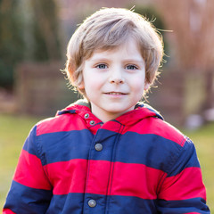 Portrait of happy little kid boy in red jacket, outdoors