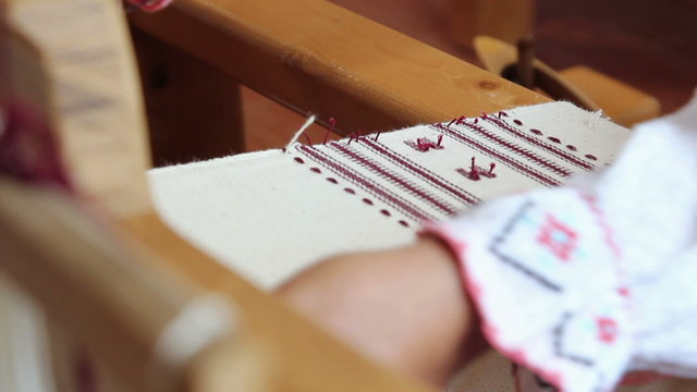 Hands of a woman weaving on an old wooden loom