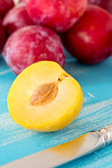 Half yellow plum on blue wooden board, with large group of red p
