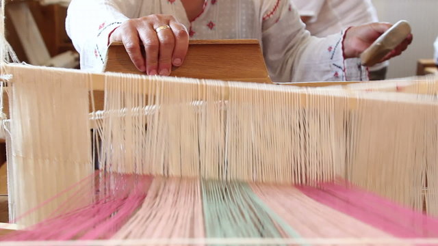 A woman weaves at an old wooden loom