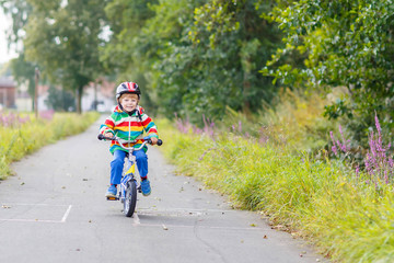 Kid boy in helmet riding his first bike, outdoors