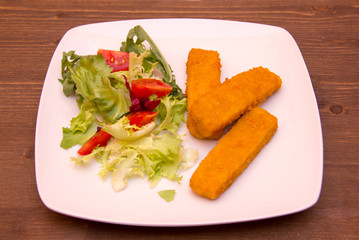 Fish fingers with salad on wooden table