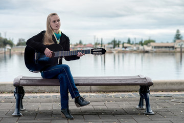 Cute blonde playing guitar while sitting on a bench