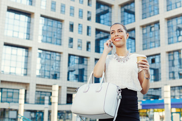 Young businesswoman holding coffee to go and talking on phone