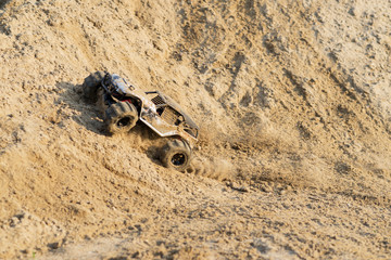 radio controlled monster truck performing a trick at high speed jumps over a large pile of sand....
