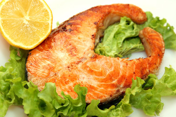 served piece of grilled salmon steak with lemon on white
