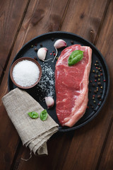 Striploin steak with salt, pepper, garlic and basil, top view