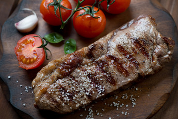 Grilled black angus steak striploin with salt and tomatoes, close-up