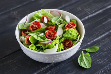 salad with fresh vegetables, garden herbs and sun-dried tomatoes in a white bowl 