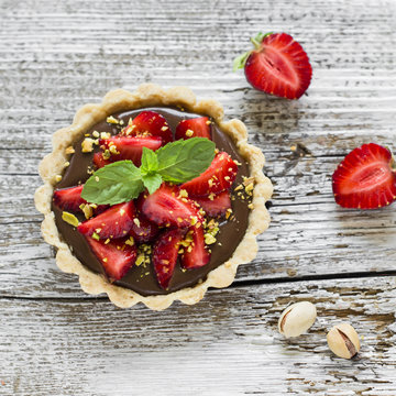 tartlet with chocolate cream, strawberries and pistachios on a light wooden background