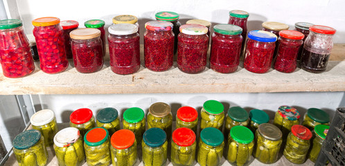 Fototapeta na wymiar Glass jars with pickles and raspberry jam on the shelves cellar