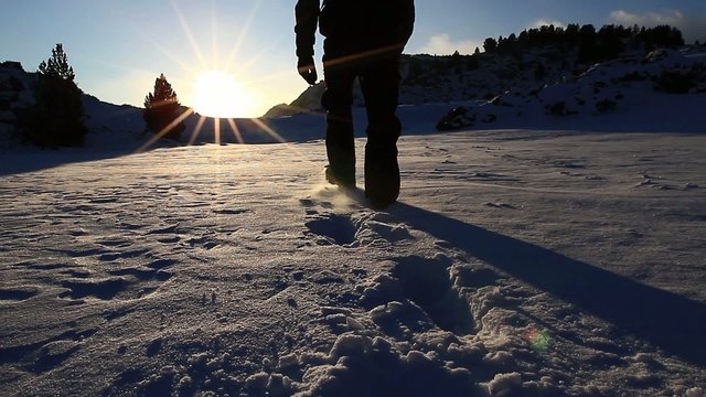 Man walking on a snow lake, in backlight he walks toward the sun