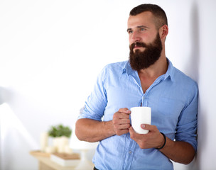 Young man  standing near wall and holding cup of coffee in