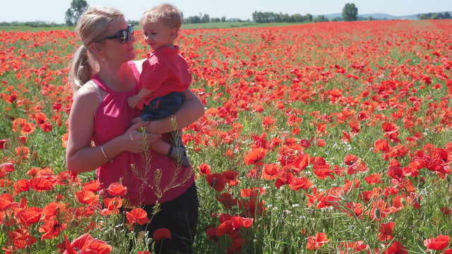 Adorable baby and mother in flourish poppy field, boy offer a flower, smell