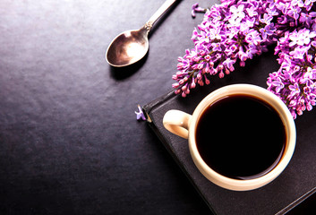 Fototapeta na wymiar Black coffee in a cup, a spoon and fresh lilac flowers