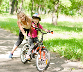 Fototapeta na wymiar happy mother teaches his daughter to ride a bike