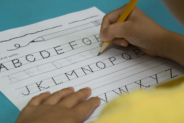 Asian boy's hand writes the letter G with a yellow pencil on a blue table