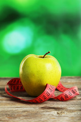 Green apple with measuring tape on grey wooden background