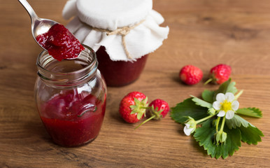 Homemade strawberry jam (marmelade) in jars on wooden background.