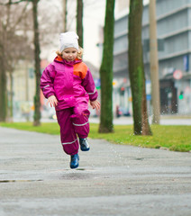 Little happy girl jumping in puddle