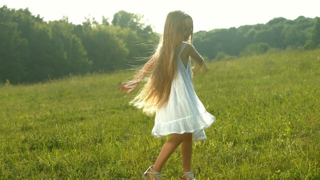 Girl in white dress dancing on a green meadow. Cheerful child.