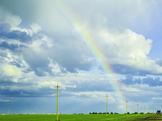 bright rainbow in the stormy sky over the green meadow